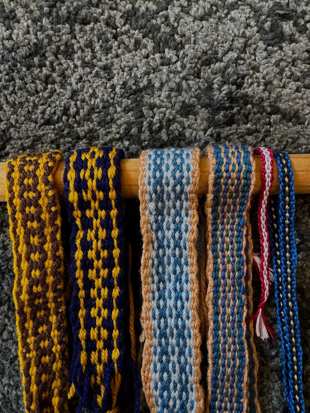 Finished woven bands in wool, hanging from a wooden dowel
