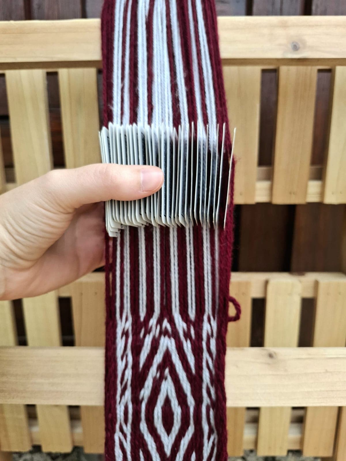 Weaving a maroon and white patterned band on tablet cards